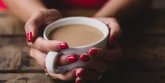 Hands holding a cup of milky coffee