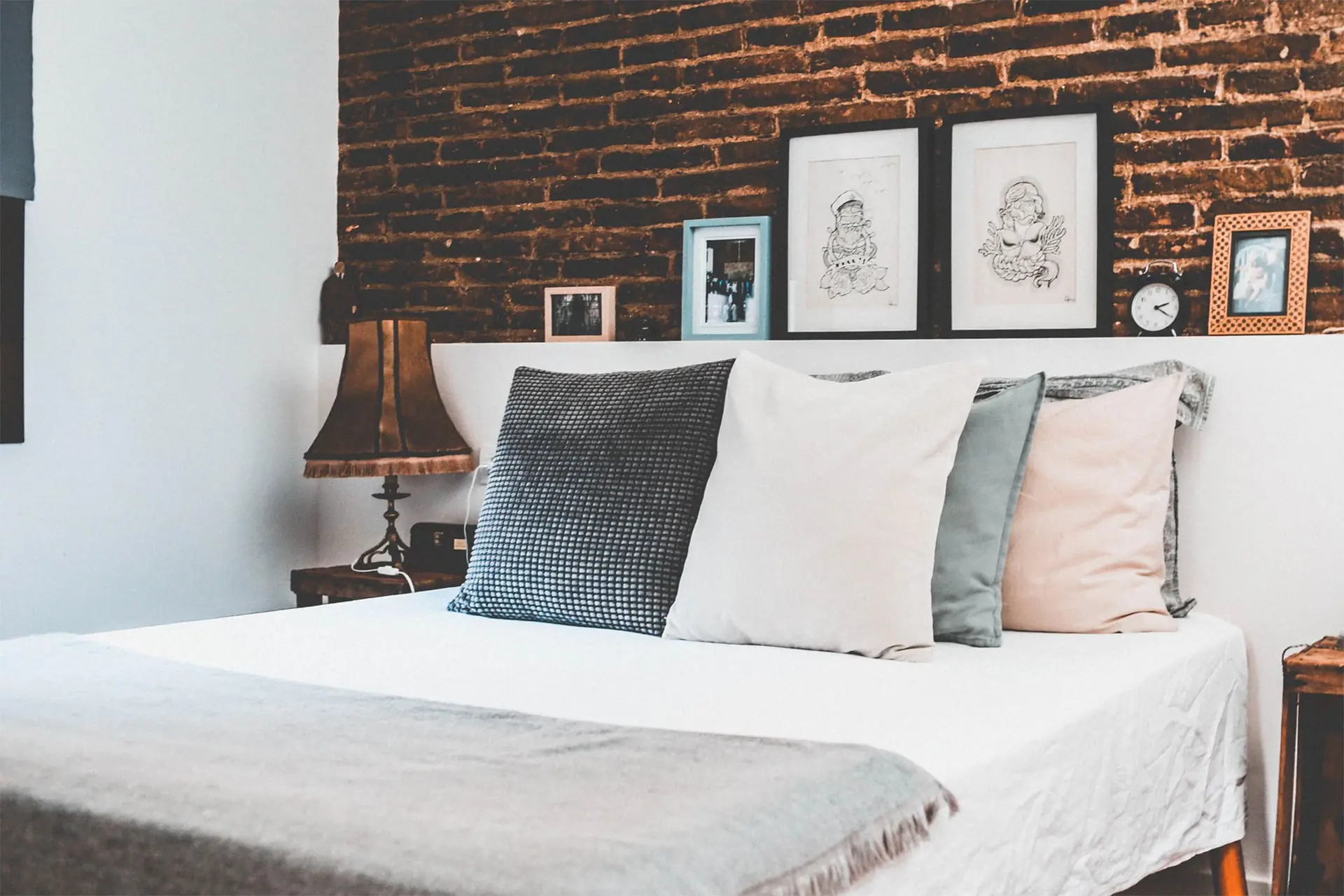 A made bed against an exposed brick wall with framed prints